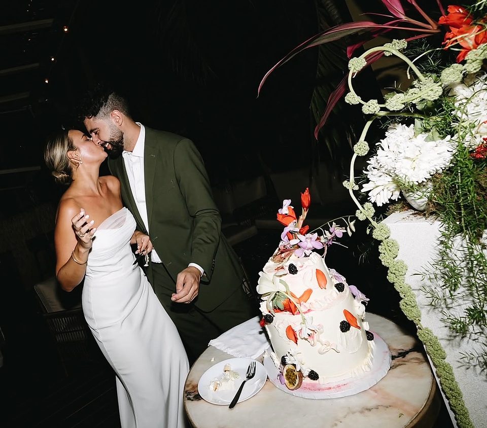 Newlyweds kissing beside a tropical floral wedding cake